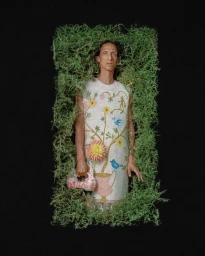 Man wearing floral mosaic tunic framed by green moss against a solid black background for AnOther Man China