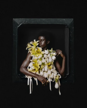 Model framed against a dark background wearing a sculptural garment of white vases and yellow lilies.