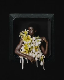 Model framed against a dark background wearing a sculptural garment of white vases and yellow lilies.