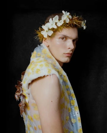 Model wearing a flower crown and floral printed translucent garment against a dark background for AnOther Man China