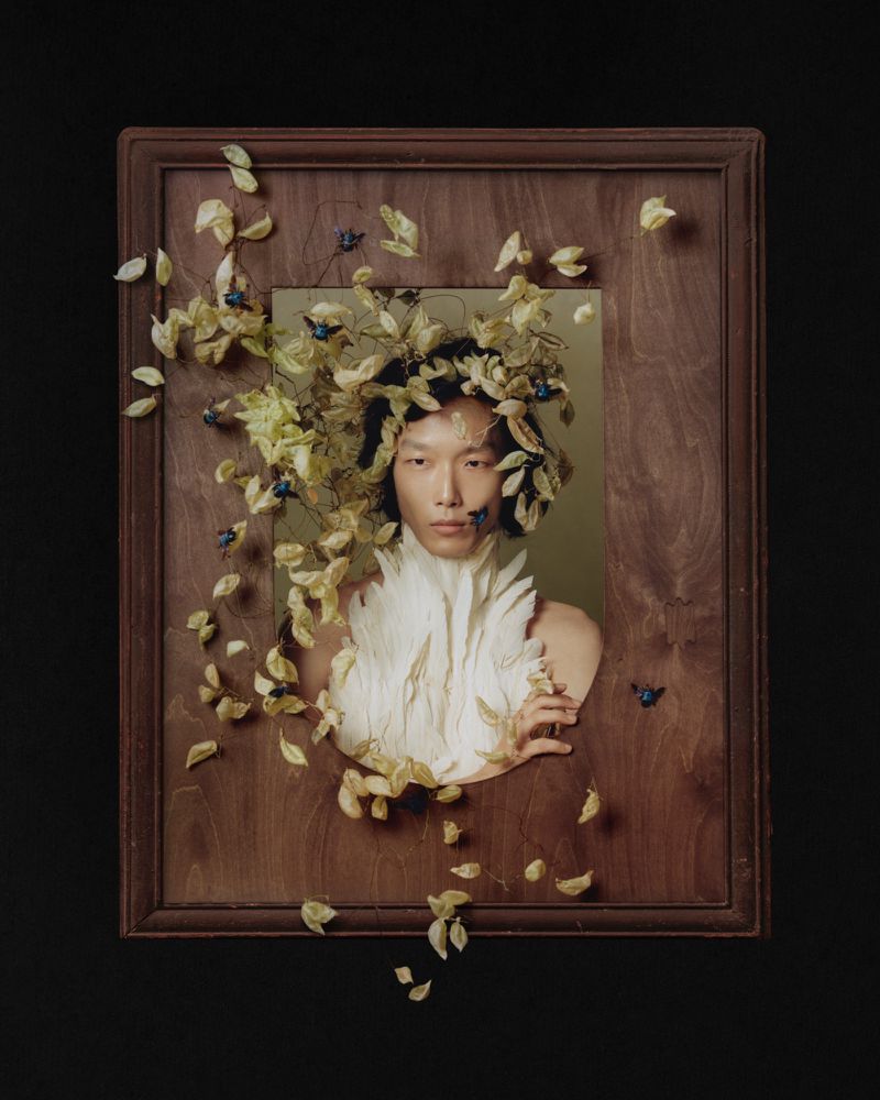 Portrait of a man framed within a wooden border, adorned with foliage and small blue insects for AnOther Man China project FLOWERS