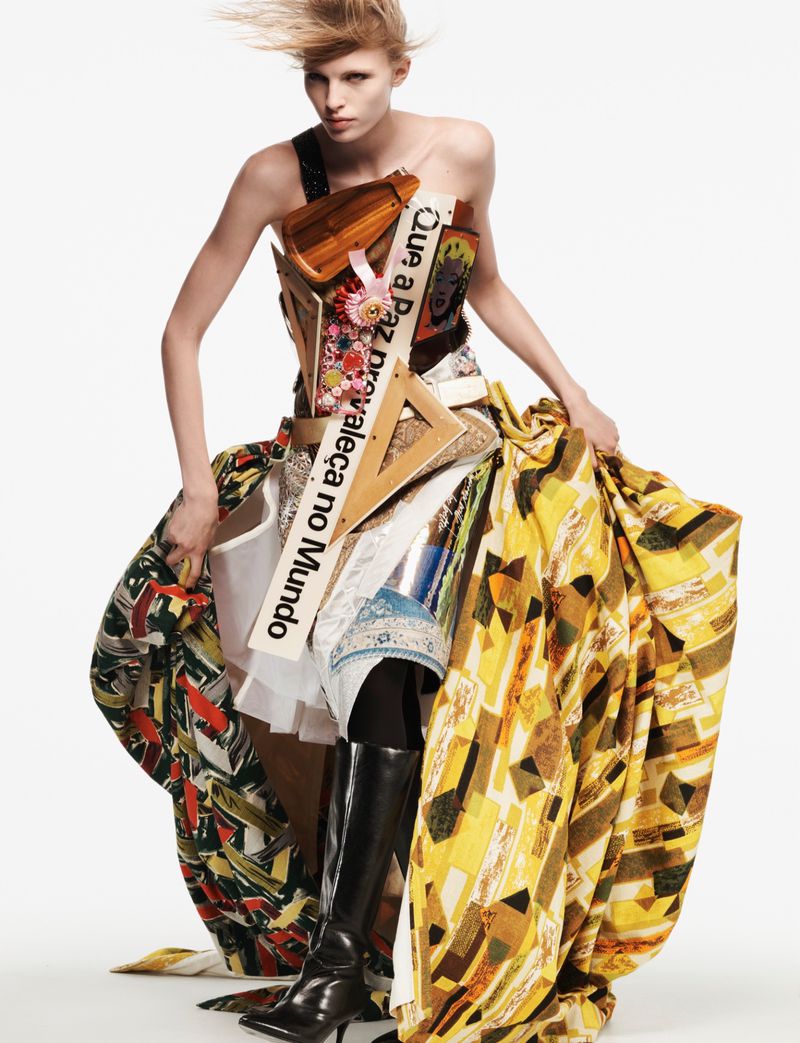 Model wearing sculptural avant-garde dress and tall black boots against a plain white background for AnOther Magazine