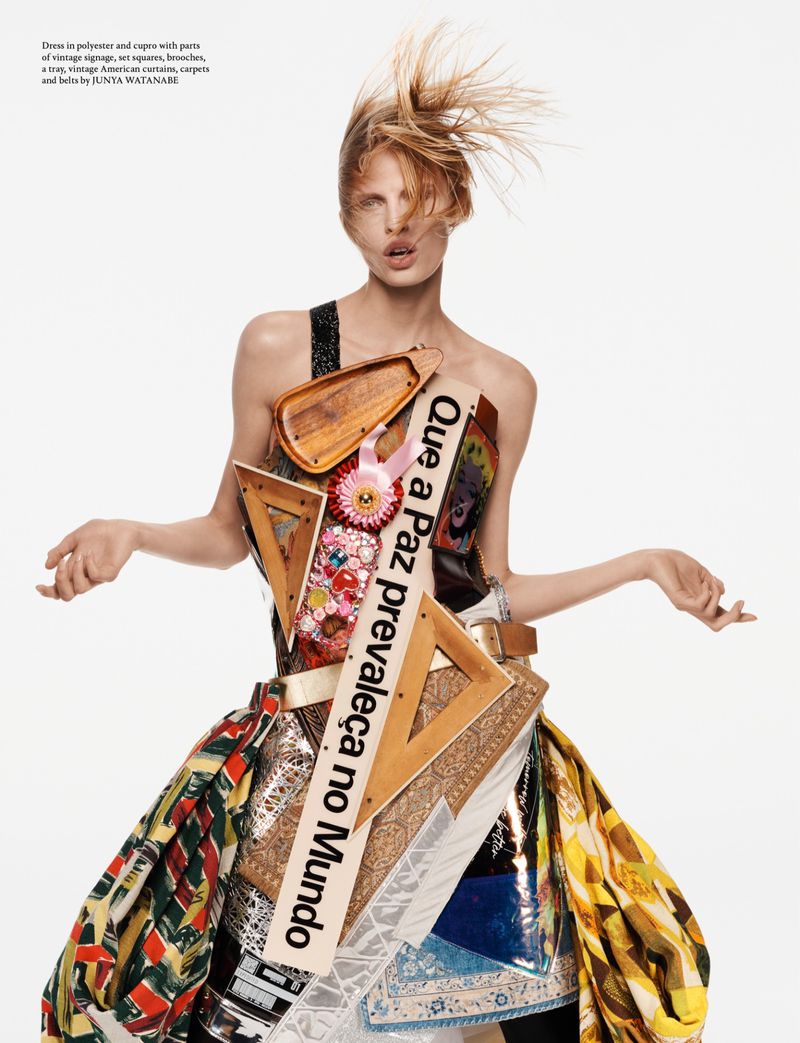 Model wearing sculptural dress constructed from vintage signage, set squares, and curtains against white background.