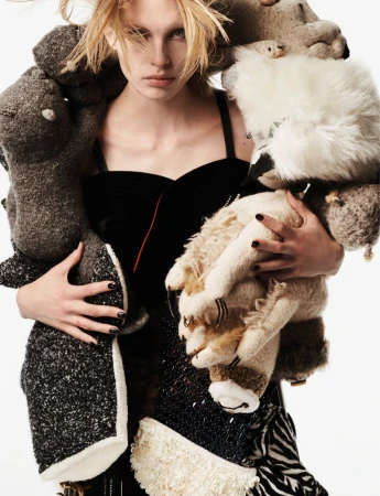 Model holding stuffed animal toys while wearing a dark outfit against a white background