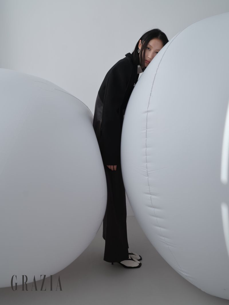 Model in black attire leaning between two large white spherical inflatables in a studio setting
