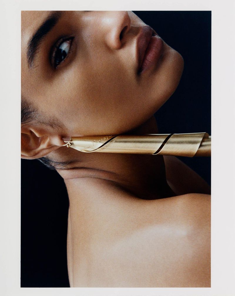 Close-up portrait of a model wearing a sculptural gold tubular earring for Elle U.S. shot by Su Mustecaplioglu.