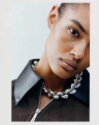 Close-up portrait of a model wearing a dark zipped collared top and silver statement necklace against a light background