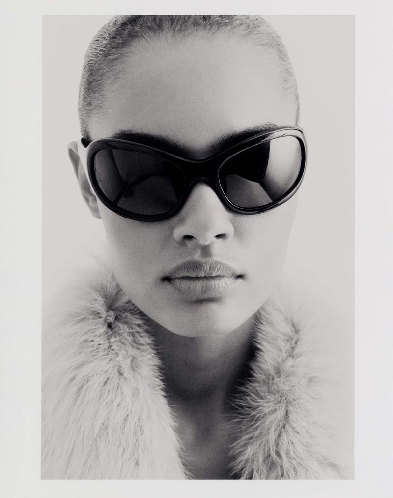 Close-up portrait of model Ana Beatriz Cortes wearing dark sunglasses and a textured collar against a white background