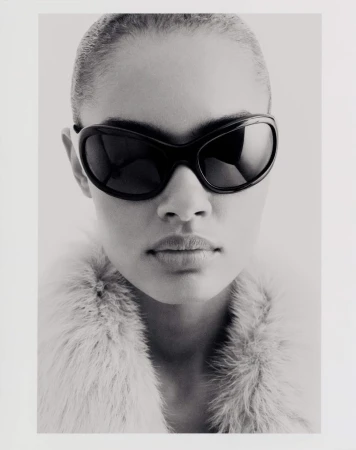 Close-up portrait of model Ana Beatriz Cortes wearing dark sunglasses and a textured collar against a white background