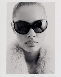 Close-up portrait of model Ana Beatriz Cortes wearing dark sunglasses and a textured collar against a white background