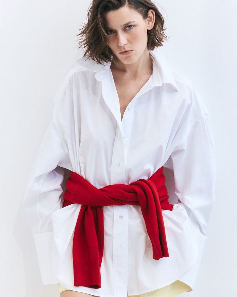 Model Vivienne Rohner in an oversized white shirt with a red sweater tied around the waist against a white background