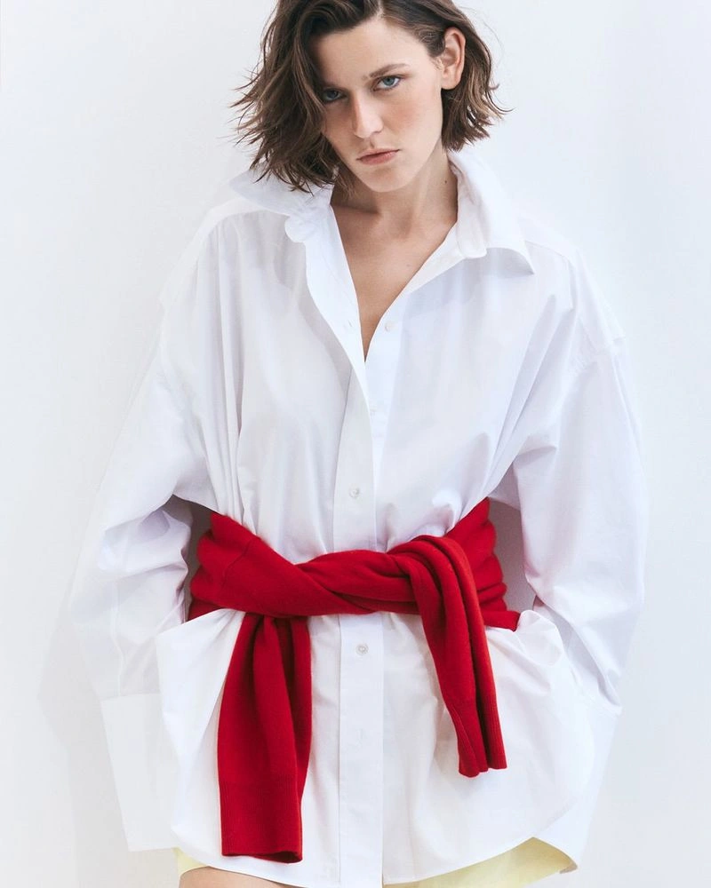 Model Vivienne Rohner in an oversized white shirt with a red sweater tied around the waist against a white background
