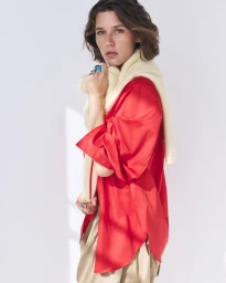 Model Vivienne Rohner in a bright red shirt and cream sweater over her shoulders against a seamless white studio background.