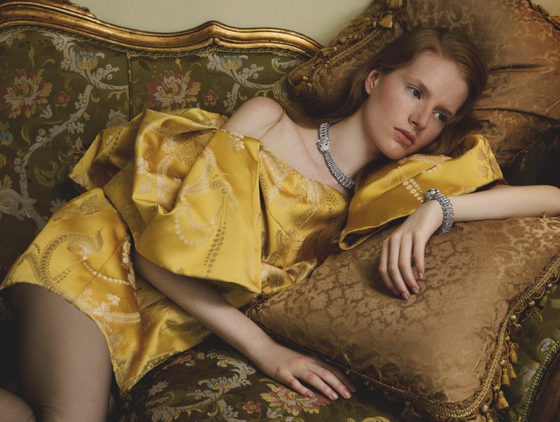 Model reclining on an ornate vintage sofa wearing a gold patterned dress and diamond jewellery for Elle Italia Special Cartier.