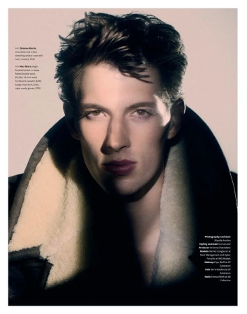 Close-up portrait of a male model wearing a dark heavy jacket with a cream shearling collar against a neutral studio backdrop
