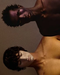 Portrait of two male models with distinct skin and makeup tones against a textured neutral background