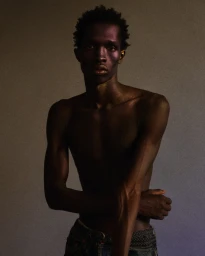 Portrait of a shirtless black man in dark trousers against a neutral background photographed by Riccardo Dubitante