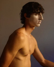 Profile portrait of a shirtless young man with dark wavy hair and white face makeup against a gradient studio backdrop.