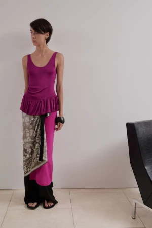 Model wearing magenta sleeveless top, patterned wrap skirt, and black trousers against a neutral interior background