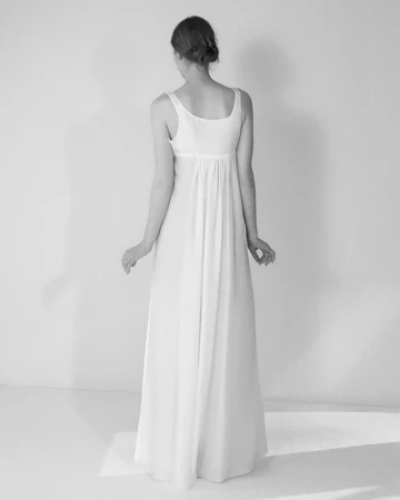Model from behind wearing a long white sleeveless dress against a white studio background