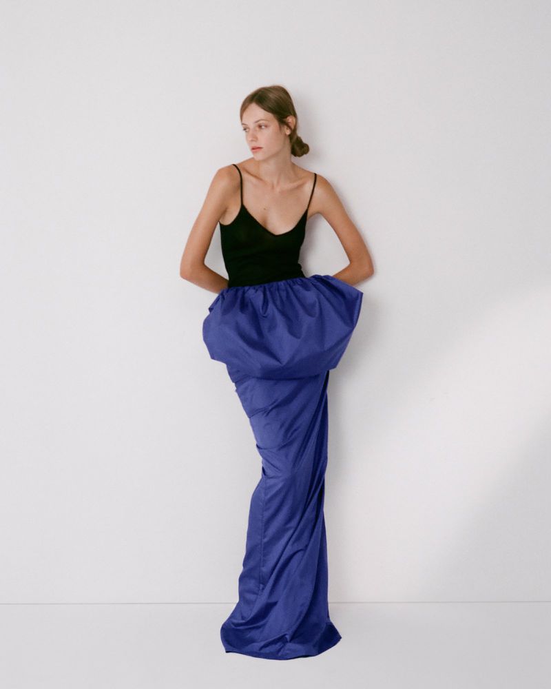 Model in black tank top and voluminous blue skirt posing against white seamless studio backdrop for Colleen Allen.
