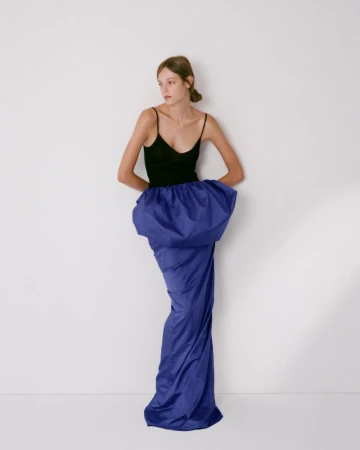 Model in black tank top and voluminous blue skirt posing against white seamless studio backdrop for Colleen Allen.