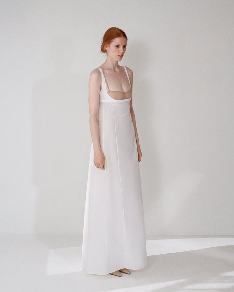 Model in a white sleeveless maxi dress standing against a plain white studio background with soft natural lighting.