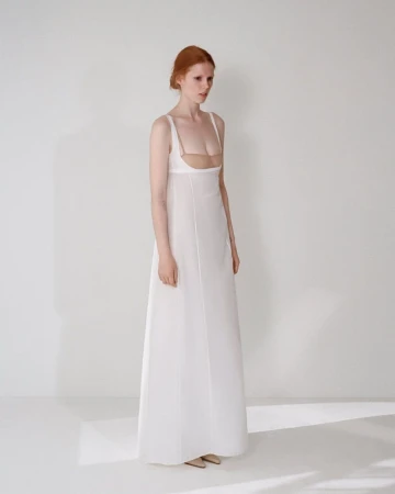 Model in a white sleeveless maxi dress standing against a plain white studio background with soft natural lighting.