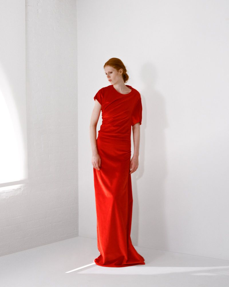 Model with red hair wearing a long red dress standing against a white seamless studio wall