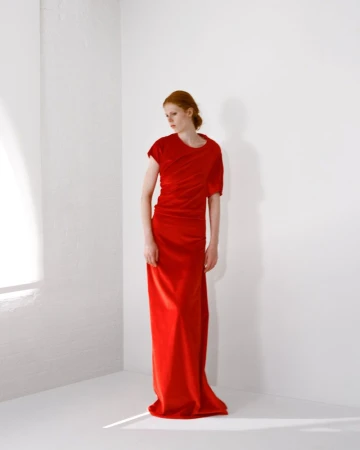 Model with red hair wearing a long red dress standing against a white seamless studio wall