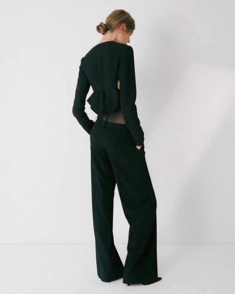 Model wearing a black tailored suit with cutout back standing against a plain white studio background.