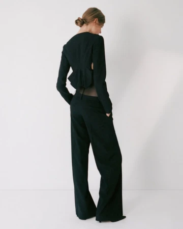 Model wearing a black tailored suit with cutout back standing against a plain white studio background.