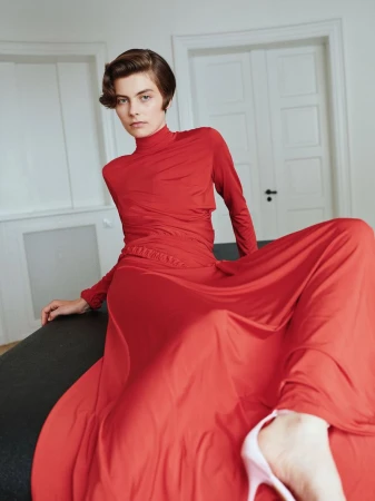 Model with short dark hair wearing a vibrant red long sleeve top and flowing red skirt in a bright white interior setting
