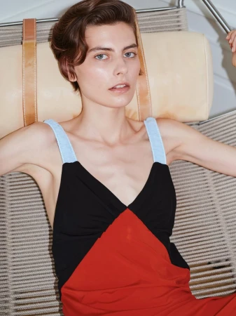 Woman with short brown hair wearing a red and black dress with light blue straps while seated