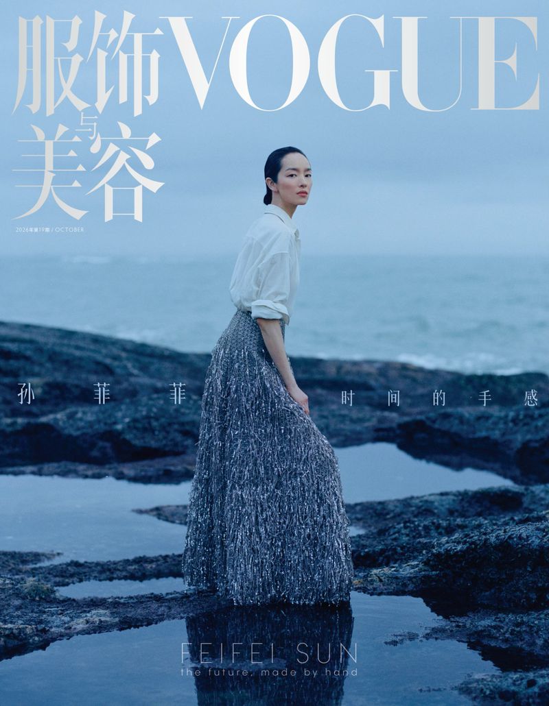 Model Feifei Sun wearing a white shirt and textured grey skirt posing on a rocky shore by the ocean for Vogue China October 2026 cover.