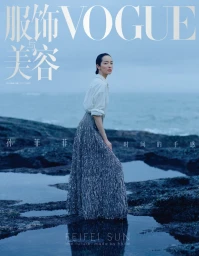 Model Feifei Sun wearing a white shirt and textured grey skirt posing on a rocky shore by the ocean for Vogue China October 2026 cover.