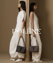 Two female models wearing white outfits holding dark leather shoulder bags against a neutral brown studio background for Polene.