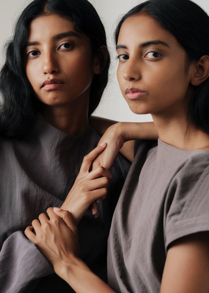 Two female models with dark hair wearing grey tops holding hands in a studio portrait by Estelle Hanania for Polène.