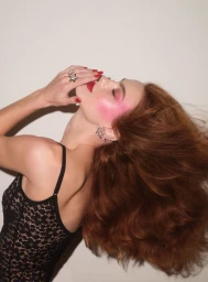 Model with vibrant red hair wearing a black lace strap top posing against a plain white background for V Magazine.