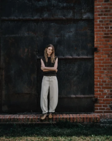 Model standing with arms crossed against a large dark metal door and red brick wall for the Closed autumn/winter campaign.