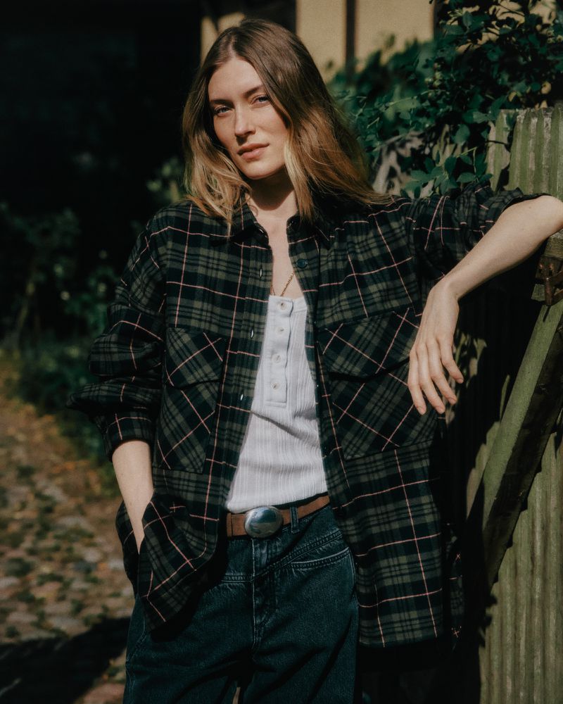 Model Caroline Lossberg leaning against a wooden fence in a plaid shirt and dark jeans for the Closed Autumn/Winter 2026 campaign.