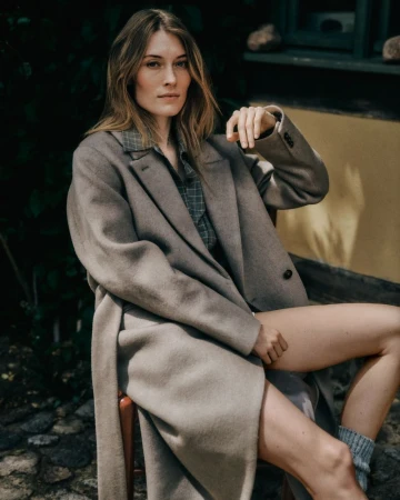 Model seated outdoors wearing a long taupe coat over a plaid shirt for Closed autumn winter campaign