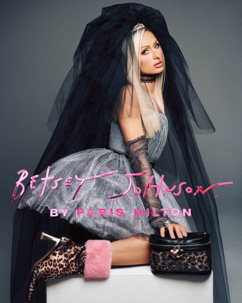 Paris Hilton in a metallic dress and black veil wearing leopard print boots with a black handbag against a grey backdrop