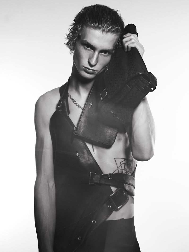 Monochrome portrait of young male model Ethan Harwood wearing a dark structured leather garment against a plain white background.