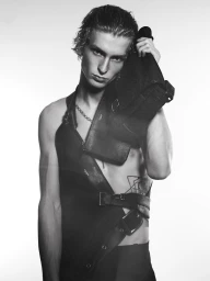 Monochrome portrait of young male model Ethan Harwood wearing a dark structured leather garment against a plain white background.