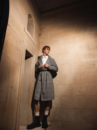 Model Ethan Harwood wearing a patterned trench coat standing in a stone hallway photographed by B Charles Johnson.