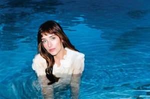 Dakota Johnson submerged in a blue swimming pool wearing a sheer white blouse for American Vogue