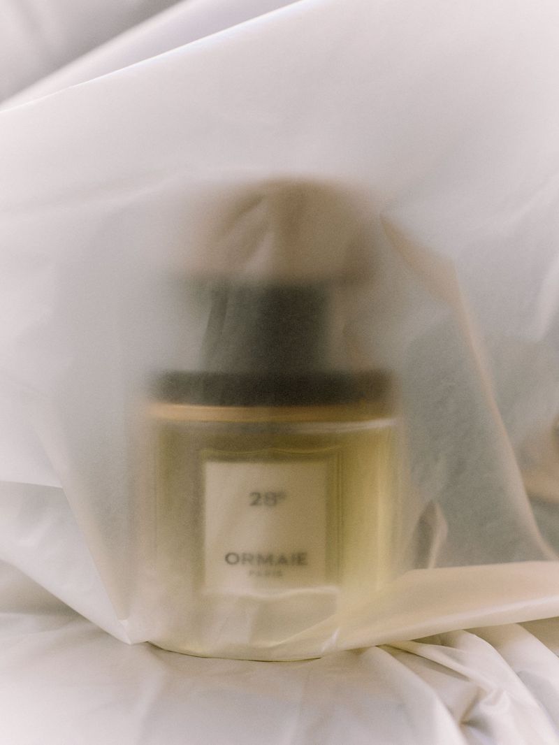 Perfume bottle encased behind translucent white fabric, creating a soft ethereal aesthetic.