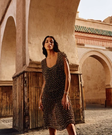 Model Nora Attal standing beneath a stone archway wearing a textured beaded dress for a magazine cover story.