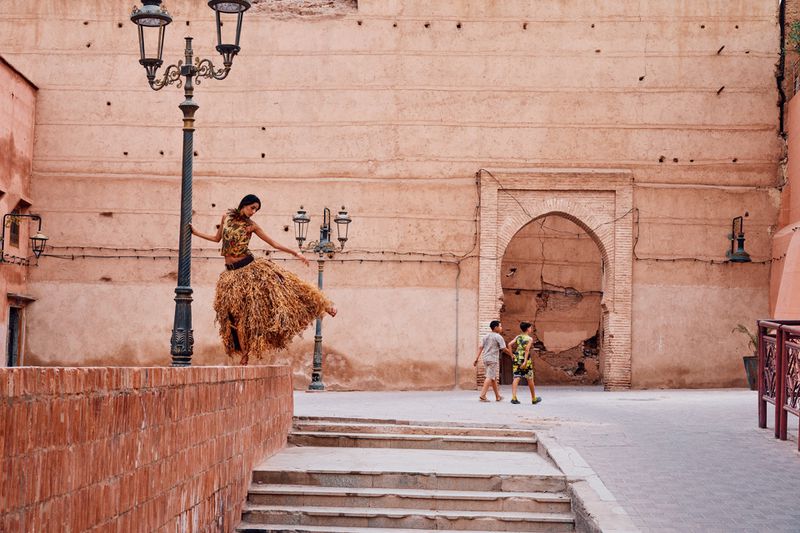 Model Nora Attal posing on a ledge beside a lamppost in front of a large textured terracotta wall for T: The New York Times Style Magazine MENA